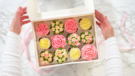 Flat lay. A womans hands gently open a white paper box, unveiling a set of gourmet cupcakes inside,...