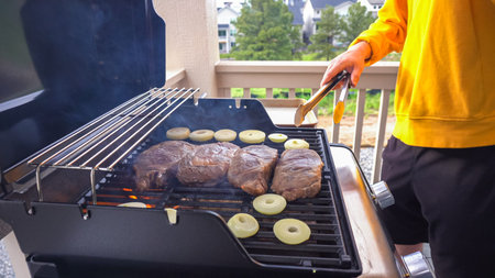 The outdoor two-burner gas grill is put to good use, sizzling with the sound and aroma of ribeye steaks and onion rings being perfectly cooked.の写真素材