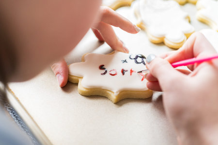 A heartwarming scene of a little girl carefully writing Sorry on sugar cookies with food coloring, the cookies beautifully flooded with white royal icing.の写真素材