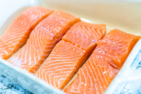 Preparing to bake fresh salmon pieces with teriyaki sauce, start by carefully arranging the raw salmon in an oven-safe ceramic baking dish.の写真素材