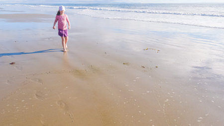 A little girl joyfully plays on the vast, empty sands of El Capitan State Beach in California during winter.の写真素材