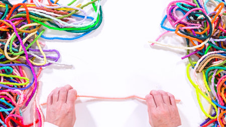 Flat lay. Hands touch a neatly organized rainbow of colorful, coiled clay bead strands against a...