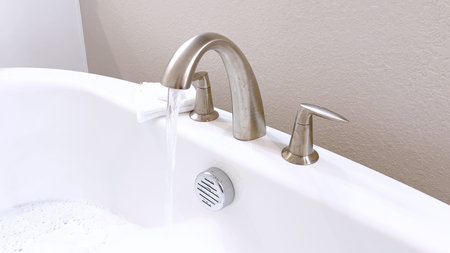 Elegant white bathtub filled with water, featuring a sleek brushed nickel faucet with water flowing...