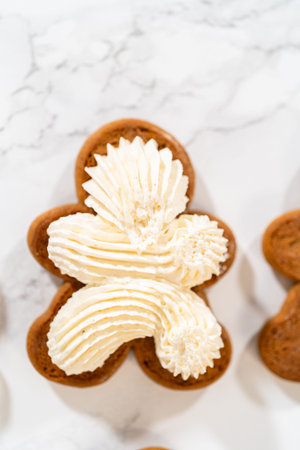 Gingerbread cookies await their second halves on a marble surface, each meticulously piped with buttercream to craft delightful sandwich treats. The precision of the piping adds a festive touch.の写真素材