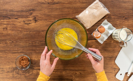 Flat lay. In a glass mixing bowl, a large hand whisk expertly blends the ingredients for a delectable gingerbread bundt cake with caramel frosting.の写真素材