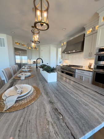 This inviting kitchen boasts a long dining table set for a family meal, with modern pendant lighting overhead and a sleek kitchen island that promises memorable gatherings and culinary adventures.の写真素材