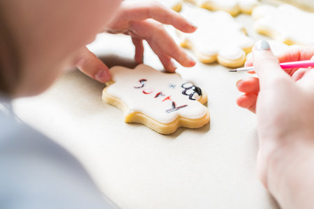 A heartwarming scene of a little girl carefully writing Sorry on sugar cookies with food coloring, the cookies beautifully flooded with white royal icing.の写真素材