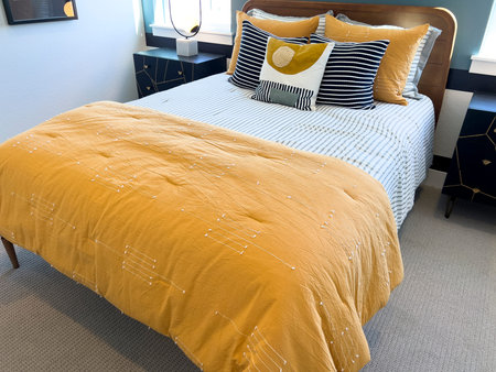 This cheerful bedroom combines crisp striped bedding with eye-catching mustard yellow throws and...
