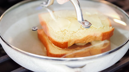 Within the sleek setting of a modern white kitchen, banana slices and brioche bread sizzle on a non-stick pan over a gas stove, setting the stage for an enticing grilled peanut butter banana sandwich.の写真素材