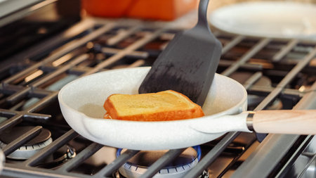 Within the sleek setting of a modern white kitchen, banana slices and brioche bread sizzle on a...