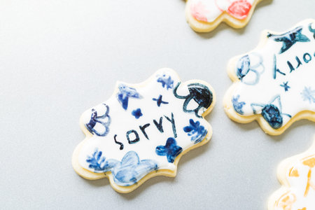 A heartwarming scene of a little girl carefully writing Sorry on sugar cookies with food coloring,...