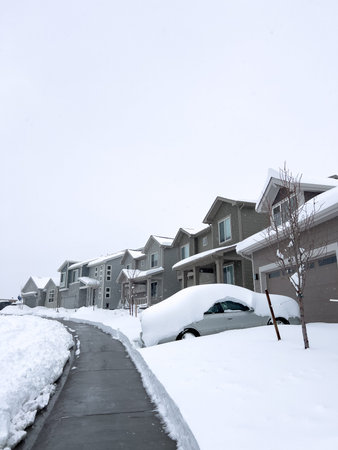Snow blankets a suburban street, where houses stand in quiet repose and driveways reveal the...