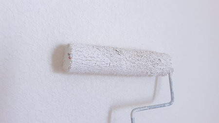 Partially painted wall with a white paint roller, showcasing the process of wall renovation and home improvement.の写真素材
