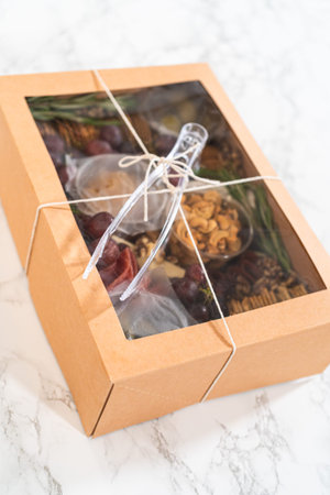 Charcuterie box featuring sliced meat, cheese, crackers, and grapes, all neatly packaged in a brown...