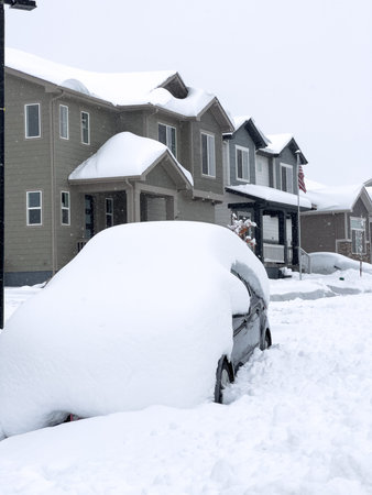 A car is buried under a thick layer of snow in front of a row of townhouses also draped with snow,...