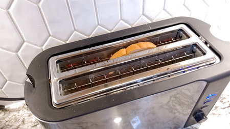 The image shows a sleek, contemporary toaster with a single slice of bread visible through its long...