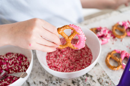 Freshly dipped and still glistening, these crunchy pretzels are lovingly adorned with pink chocolate and a scattering of colorful sprinkles, promising a feast for the senses.の写真素材