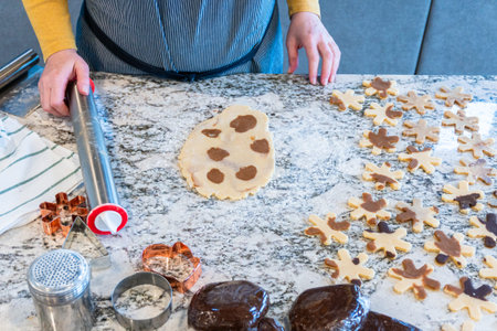 In a contemporary white kitchen, gingerbread cookie dough is skillfully rolled out, setting the...