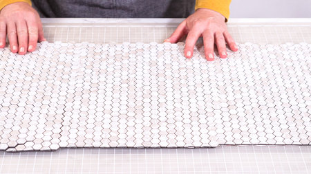 In the process of mounting peel and stick mosaic tiles onto a foam board, perfect for enhancing a...
