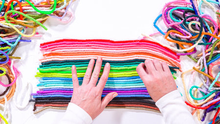 Flat lay. Hands touch a neatly organized rainbow of colorful, coiled clay bead strands against a contrasting white surface.の写真素材
