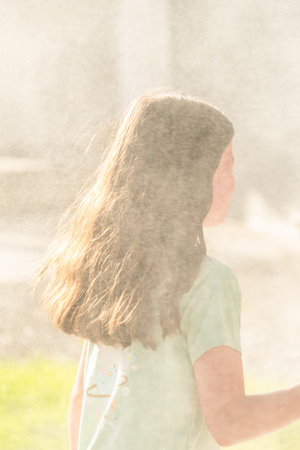 A joyful young girl gleefully gets soaked in refreshing water mist during a hot summer day.の写真素材