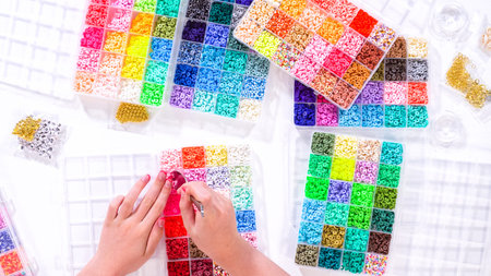 Flat lay. Womanâ€™s hands gracefully poised over a collection of beads, sorted by color in...