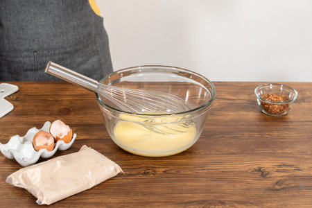 In a glass mixing bowl, a large hand whisk expertly blends the ingredients for a delectable bundt...