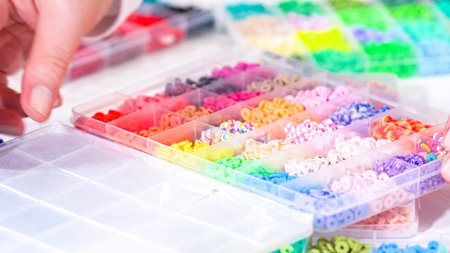 Woman hands gracefully poised over a collection of beads, sorted by color in transparent organizers....
