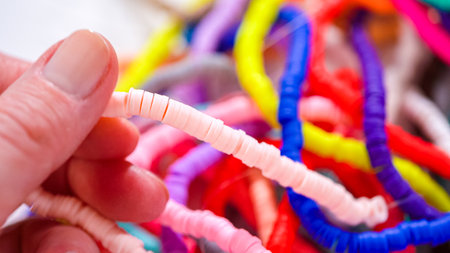 Hands meticulously organize a kaleidoscope of multicolored, patterned clay beads, intricately coiled and laid out against a stark white backdrop.の写真素材