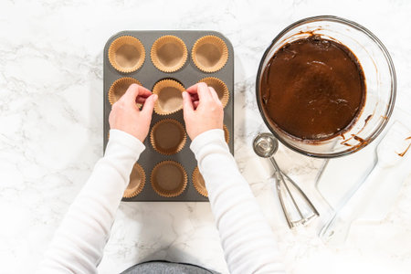 Flat lay. Getting ready to bake delicious chocolate cupcakes, we carefully line the cupcake pan with...