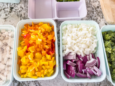 Chopped Vegetables in Containers Ready for Cooking on a Marble Countertop. High quality photo A variety of chopped vegetables, including yellow bell peppers, red onions, and white onions, are neatly arranged in containers on a marble countertop. Broccoli and other ingredients are prepared for a meal.の写真素材
