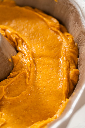 Pouring cake batter into a bundt cake pan, ready to bake a delicious homemade pumpkin bundt cake.の写真素材