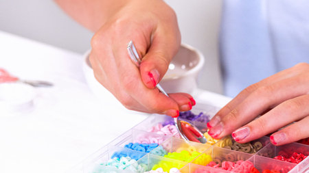 Delicate fingers of a young girl navigate through a treasure trove of bright, multicolored beads,...