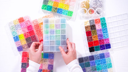 Flat lay. Womanâ€™s hands gracefully poised over a collection of beads, sorted by color in...