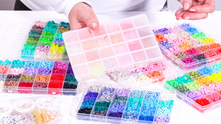 Womanâ€™s hands gracefully poised over a collection of beads, sorted by color in transparent...