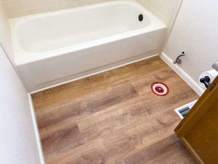 A bathroom under renovation featuring new vinyl flooring and a removed toilet. The base plumbing and toilet paper holder remain, while the area is prepared for the next installation step.の写真素材