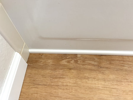 White vinyl baseboards and trim pieces are neatly stacked against a wall, prepared for installation in a room with wooden flooring. The renovation project is in progress, ready to complete the room finishing touches.の写真素材