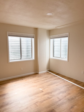 A room with fresh wooden flooring, two windows, and white vinyl baseboards positioned along the...