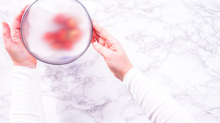 Flat lay. Strawberries, freshly washed and dried, are neatly stored in a glass bowl lined with a paper towel and securely covered with plastic wrap to maintain freshness.の写真素材