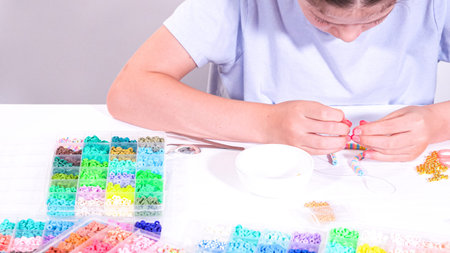 Delicate fingers of a young girl navigate through a treasure trove of bright, multicolored beads,...