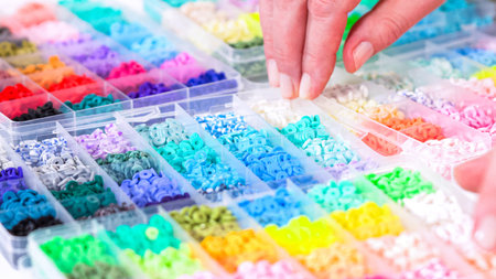 Womanâ€™s hands gracefully poised over a collection of beads, sorted by color in transparent...