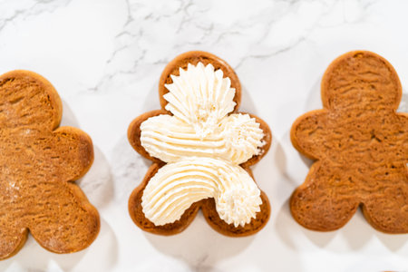 Gingerbread cookies await their second halves on a marble surface, each meticulously piped with buttercream to craft delightful sandwich treats. The precision of the piping adds a festive touch.の写真素材