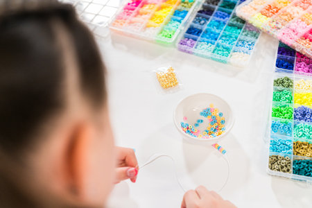 Little girl enjoys crafting colorful bracelets with vibrant clay beads set.の写真素材
