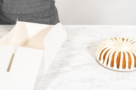 The Carrot Bundt Cake is carefully packaged into a white paper bundt cake box, ready for gifting or sharing.の写真素材