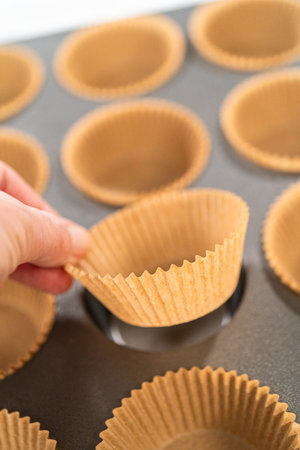 Getting ready to bake delicious chocolate cupcakes, we carefully line the cupcake pan with paper liners, ensuring a delightful treat awaits.の写真素材