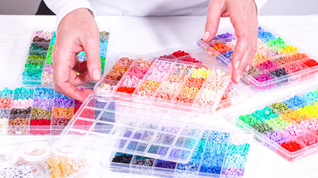 Womans hands gracefully poised over a collection of beads, sorted by color in transparent...