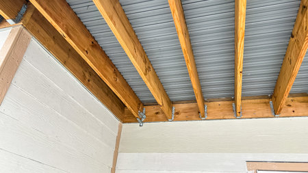 Exposed wood beam ceiling structure supporting a corrugated metal roof in a covered outdoor patio area of a newly built residential home. The design showcases natural wood framing and metal roofing components, providing durability and modern aesthetics.の写真素材