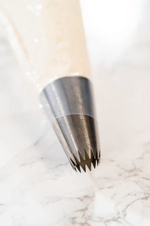 Poised on a marble surface, the piping bag's star nozzle is filled with creamy eggnog buttercream,...