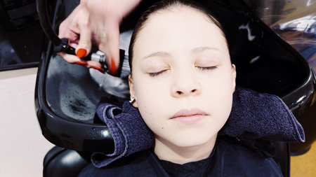 Client relaxes while having her hair washed in a salon basin, the stylists hands gently massaging...