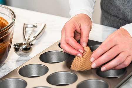 Getting ready to bake delicious chocolate cupcakes, we carefully line the cupcake pan with paper liners, ensuring a delightful treat awaits.の写真素材